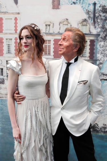 Valentino in a white jacket with his arm around Anne Hathaway, who is wearing a white dress