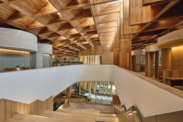 Wood-panelled atrium with triangular ceiling beams and a staircase overlooking a plant-filled courtyard