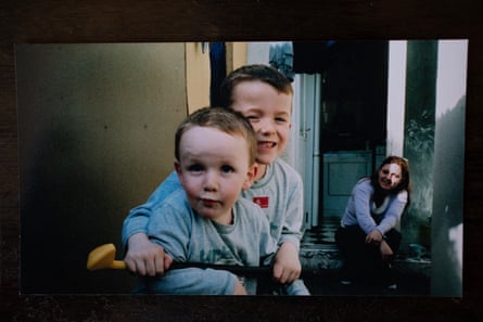 Picture of two young boys sitting together in a back yard, with their mum sitting on the doorstep behind them