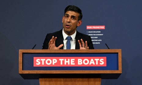 Rishi Sunak making a point with raised hands at a press conference in Downing Street in March, behind a podium bearing the slogan 'Stop the boats'.