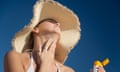 A woman in a wide-brimmed hat applies sunscreen to her neck