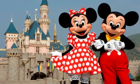 Micky and Minnie mouse, with big black ears, Minnie is a red and white polka dot dress, and Mickey in yellow bow tie and red pants, in front of a big white castle.