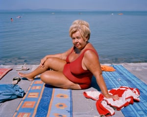 An older woman in a swimsuit sitting on a beach towel by the sea in Hungary