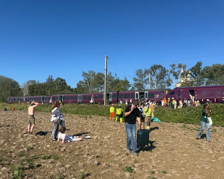 Passengers on the ground lying next to the railway tracks with the damaged trains visible in the distance