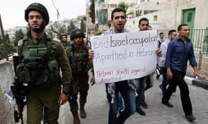 A Palestinian holds a placard reading "End Israeli occupation. Apartheid in Hebron"