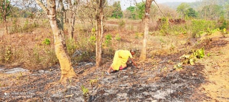 A woman stoops over to collect something from the ground, which is blackened and burned.