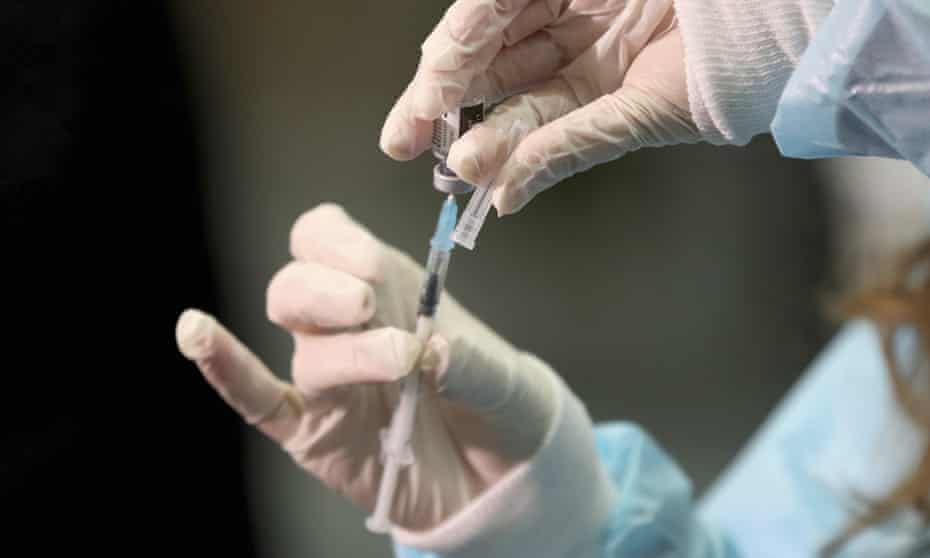 A close up of a pair of hands, in white medical gloves, drawing vaccine into a syringe from a vial