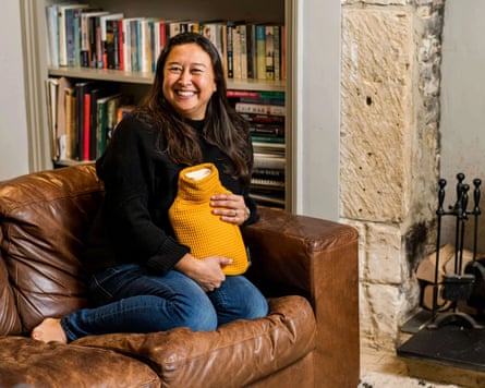 A woman sits on a sofa, cuddling the CosyPanda Majestic Mustard Waffle hot-water bottle