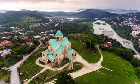 Aerial view of Bagrati Cathedral in Kutaisi, at the top of a hill, with a view sloping down into a valley with houses and a river