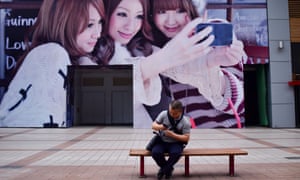 A man looks at his mobile phone in front of a huge poster in Beijing