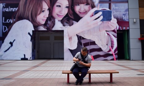 A man looks at his mobile phone in front of a billboard on a business street in Beijing