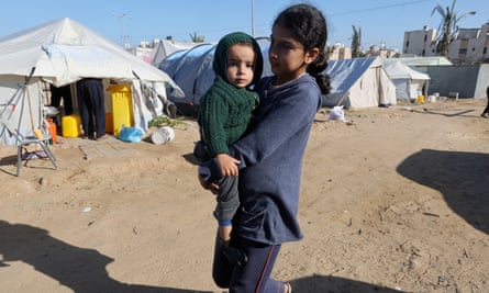 A Palestinian girl carries a child in a camp in Rafah in the southern Gaza Strip