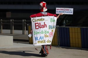 A person protesting with a placards saying 'Climate, blah blah' and 'Waging war is ... climate suicide'