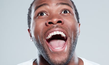 Afro american man looking away and laughing, against blue-gray background.