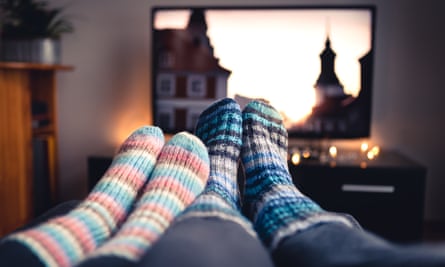 Couple with woolly socks lie together on a sofa at home using online streaming service.