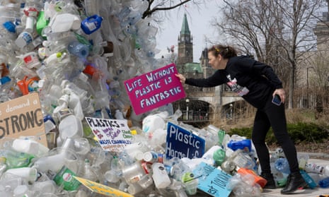 A woman placing a sign reading 'Life Without Plastic Is Fantastic' on an installation of plastic bottles in Ottawa, Canada