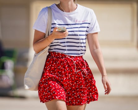 A passerby wears a white striped T-shirt, a red short floral print skirt and a tote bag in Paris, France