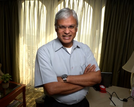 Ashley Tellis with arms folded in a grey shirt in front of yellow curtains
