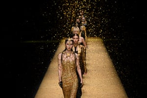 Female models walk down a gold-coloured catwalk wearing sparkly, gold-coloured designs. Golden glitter falls from above