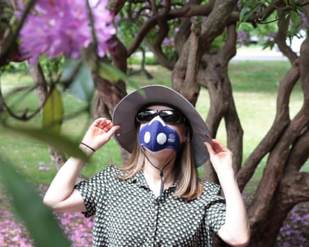 Jane Hoskyn wears a Hepa filter mask and sun hat in a wooded area with flowers in the foreground.