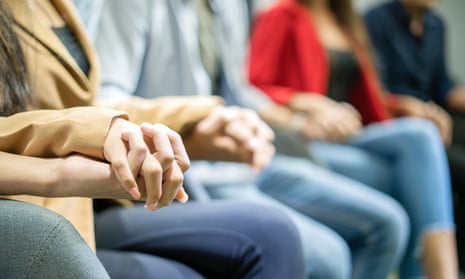 A view of women and men, showing only their legs, in group therapy holding hands in unity.