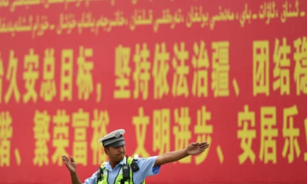 A police officer gesturing in front of a propaganda billboard urging ‘the maintenance of rule of law in Xinjiang’