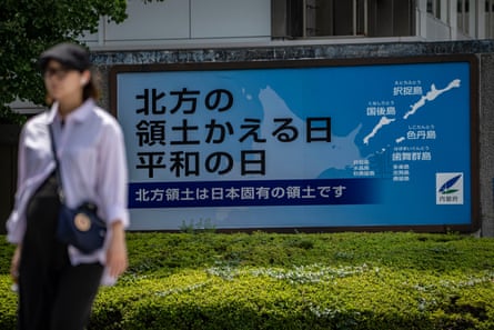 A woman walks past a sign above a green hedge which has a map of the islands on it.