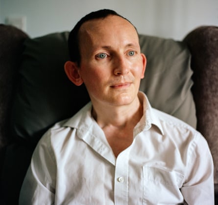 Head shot. of Mike Sumner, who is living with cancer, in white shirt, sitting on a sofa