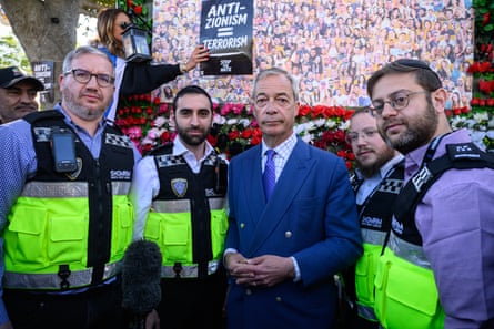 Nigel Farage stands next to men wearing hi-vis security jackets