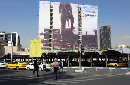 Pedestrians in Tehran cross a street beneath a huge anti-US billboard