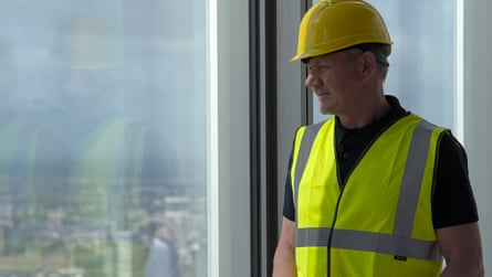 Gordon Ramsay in hard hat and hi-viz jacket looking out at the London view from window