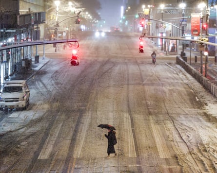 A woman crosses the road in a snowy street