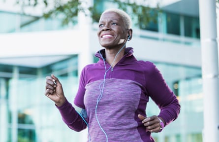 A woman walking in gym clothes, with earphones, looking happy.