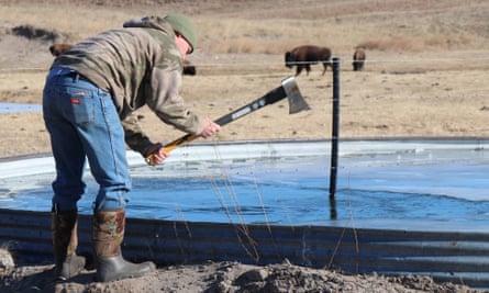 A man uses an axe to break ice on a shallow pool of water.
