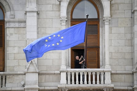 A man hangs the EU flag on a flag pole leaning out from a gothic-style building