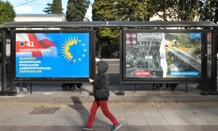 A person walks past a Georgian Dream party campaign poster in Tbilisi that compares destroyed buildings in Ukraine with Georgia.