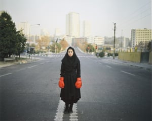 Woman standing in middle of road with no cars, dressed in black Islamic clothes and red boxing gloves