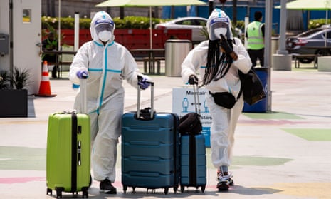 Two passengers in full protective gear push their luggage as they arrive in the rideshare zone of the LAX airport to catch a ride in Los Angeles, California.