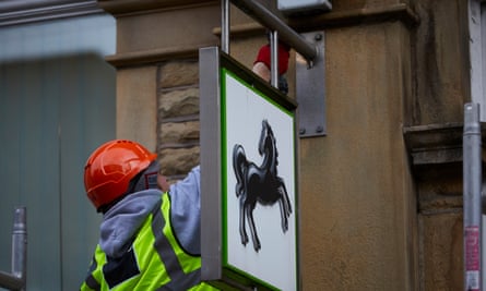 A workman on a ladder unbolting a Lloyds sign from the side of a building