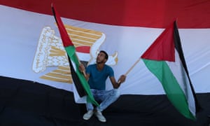 A man holds Palestinian flags in front of an Egyptian flag in the Gaza Strip