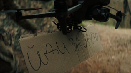 Drone carrying a piece of cardboard with writing on it.