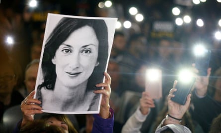 A person holds up an image of Caruana Galizia at a protest as others shine torches
