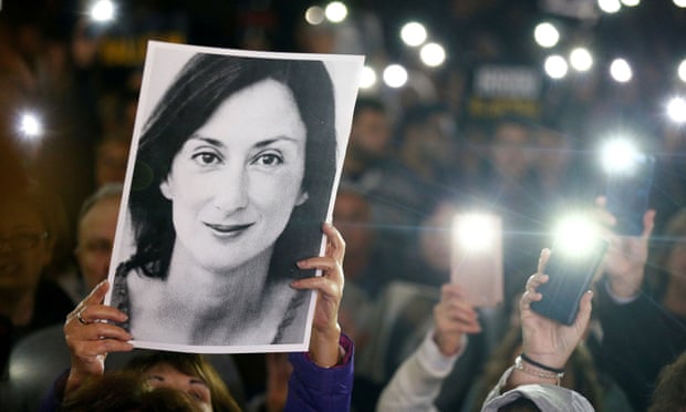 A person holds up an image of Caruana Galizia at a protest as others shine torches