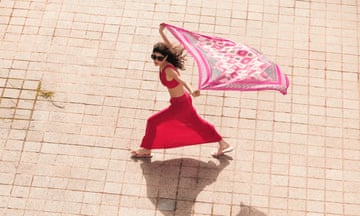 A female model holding a pink scarf that is blowing in the wind