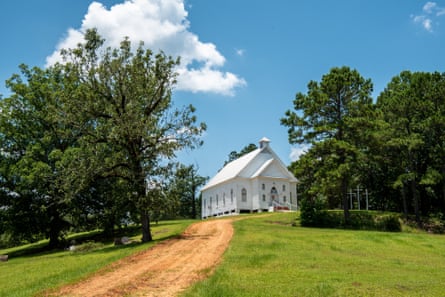 a white-frame church in a grassy field surrounded by trees