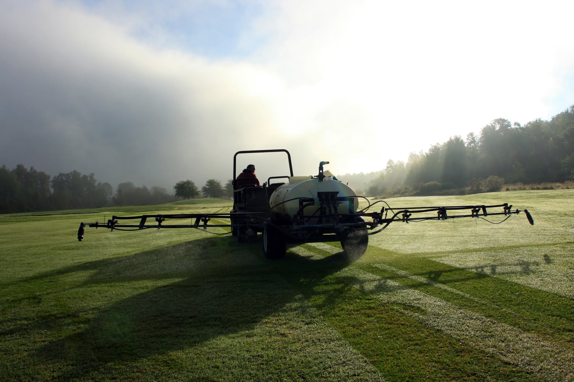 A man sprays pesticides on a golf course.