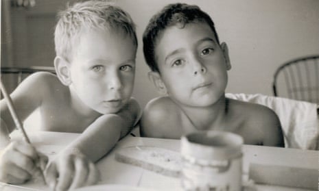Two young boys side by side, one blond with his arms stretched on the table, one dark, both looking at the camera