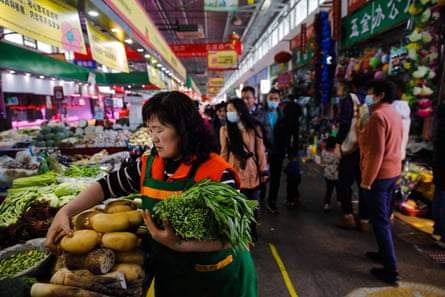 A woman picking up vegetables at a market stall in China