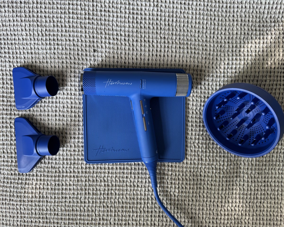 Hershesons’ The Great hairdryer on its heat proof mat and two nozzle heads and a diffuser attachment. The dryer and parts are all bright blue.