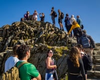 Walkers queue up a rocky summit path on Yr Wyddfa (Snowdon) under clear skies
